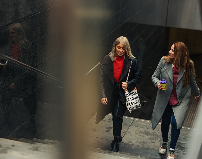 two_girls_walking_up_the_stairs_of_station_with_bag_and_cup